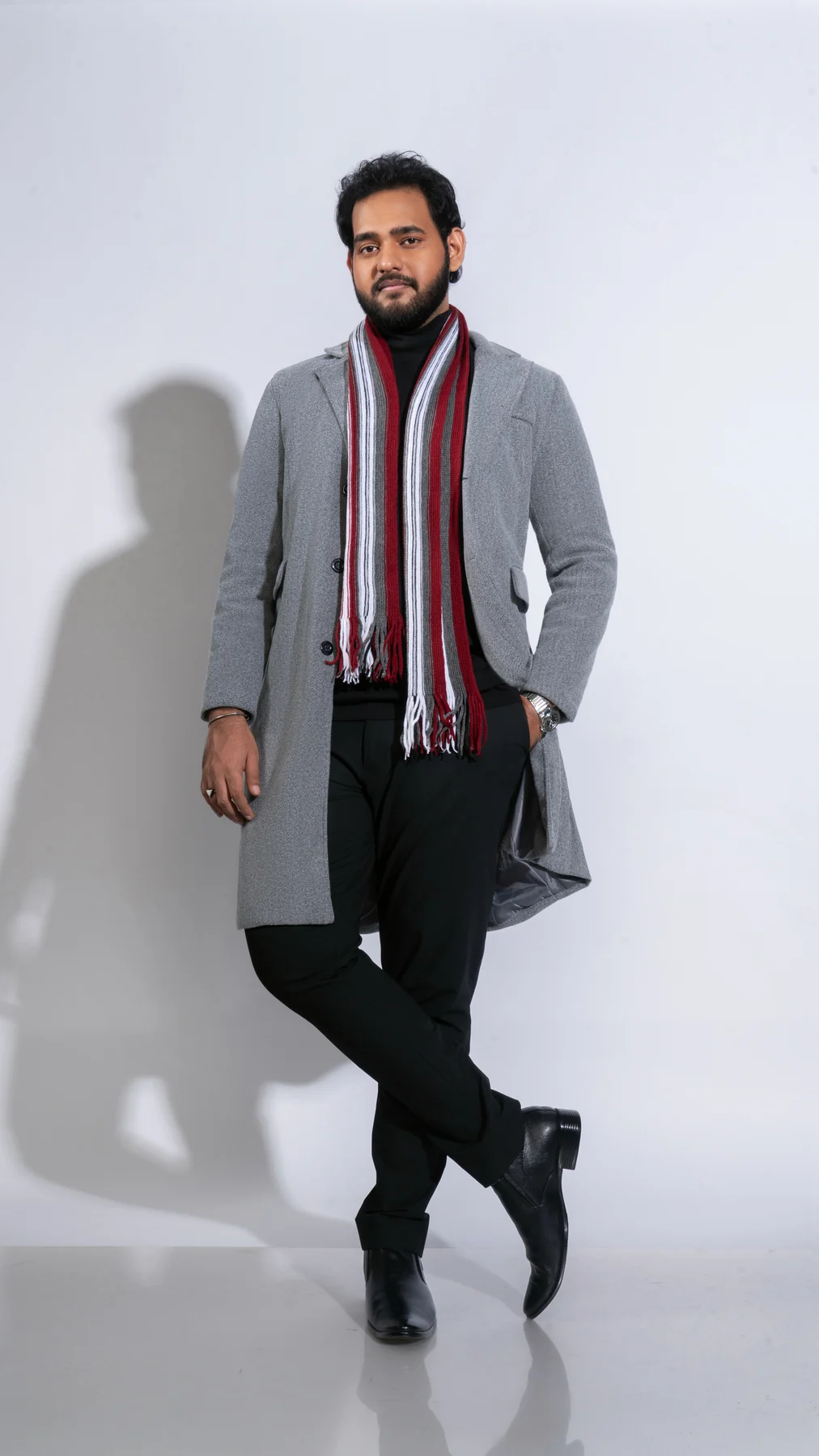 Alii Khan standing in a gray coat and striped scarf