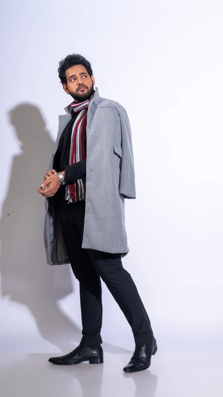 Alii Khan standing side-on in a gray coat with a striped scarf