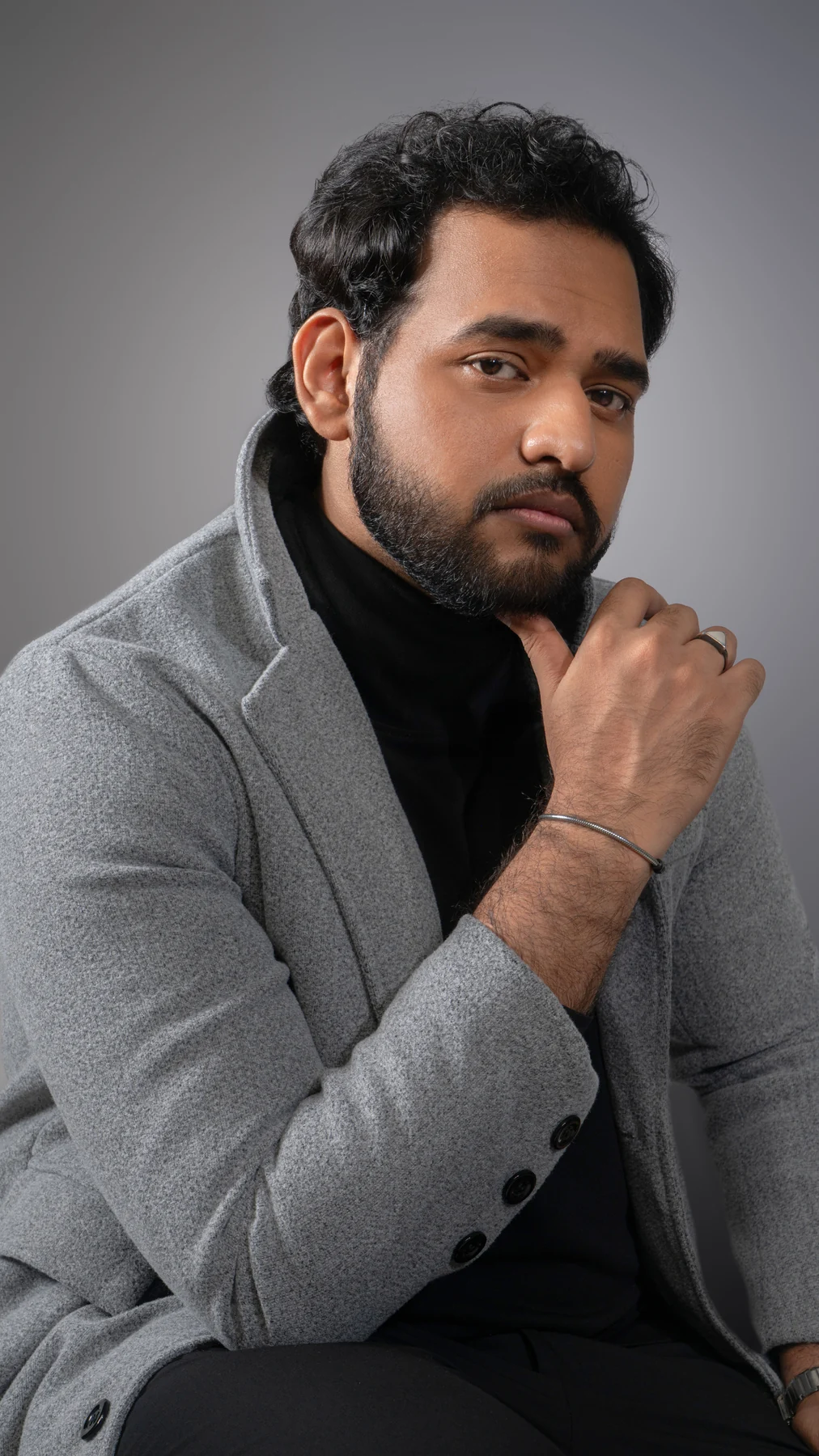 Alii Khan in a gray blazer, seated with a hand near his chin