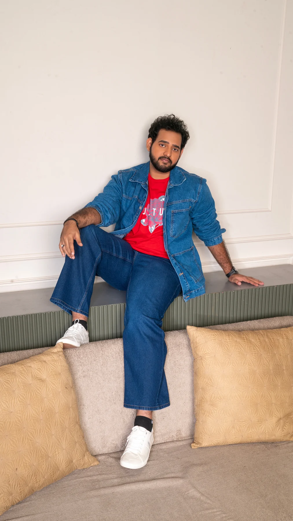 Alii Khan seated in a blue suit with a red shirt and white shoes